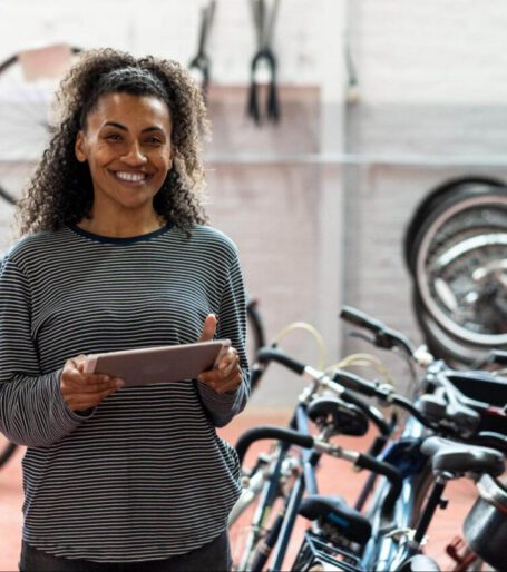 A woman smiling holding an ipad in front of some bikes